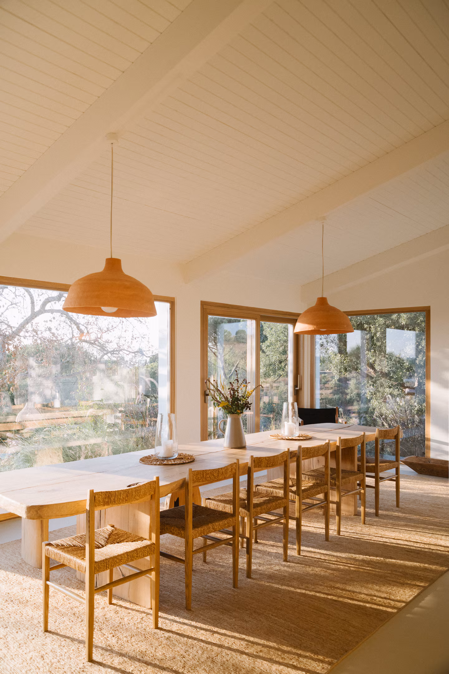 Long dining room beneath pitched ceiling, windows onto the trees
